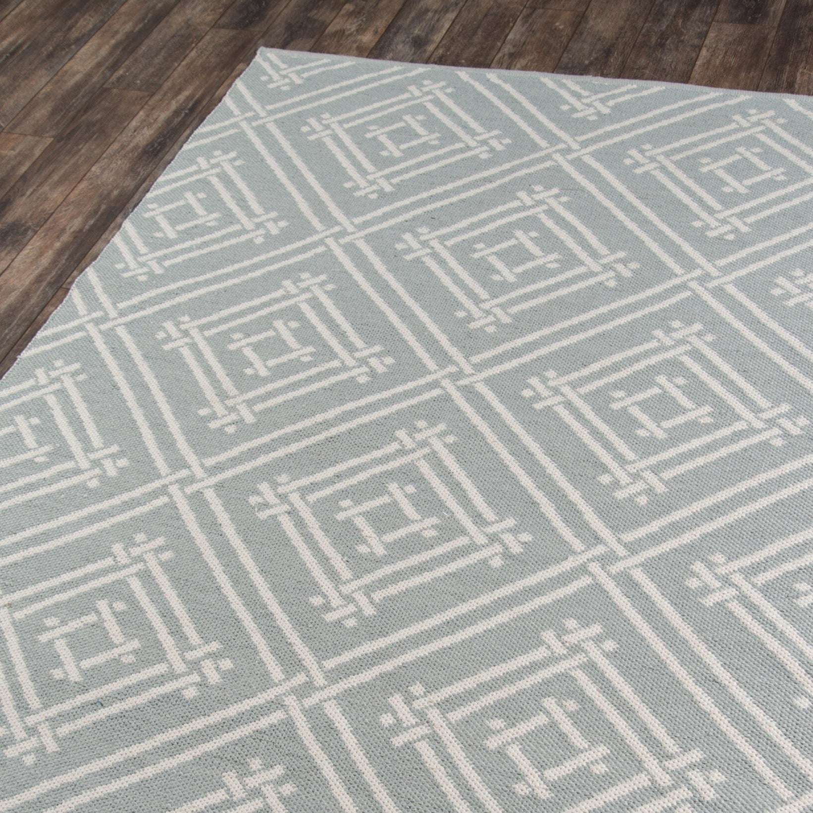 Geometric patterned area rug with white square lattice design on a wood floor, modern woven rug for living room or bedroom.