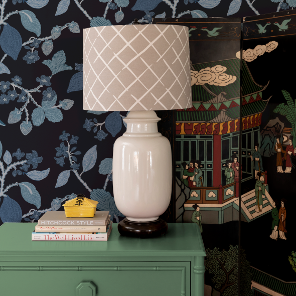 a beige lamp on a green chest of drawers against a blue patterned wallpaper wall.