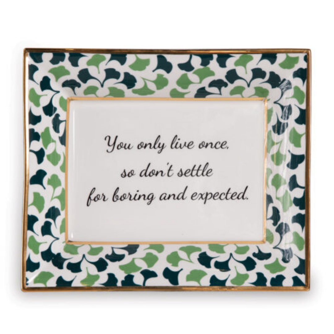 A rectangular porcelain trinket tray with a blue-and-green gingko-leaf patterned trim and gilt edging. The tray has text inside that reads 'You only live once, so don't settle for boring and expected.