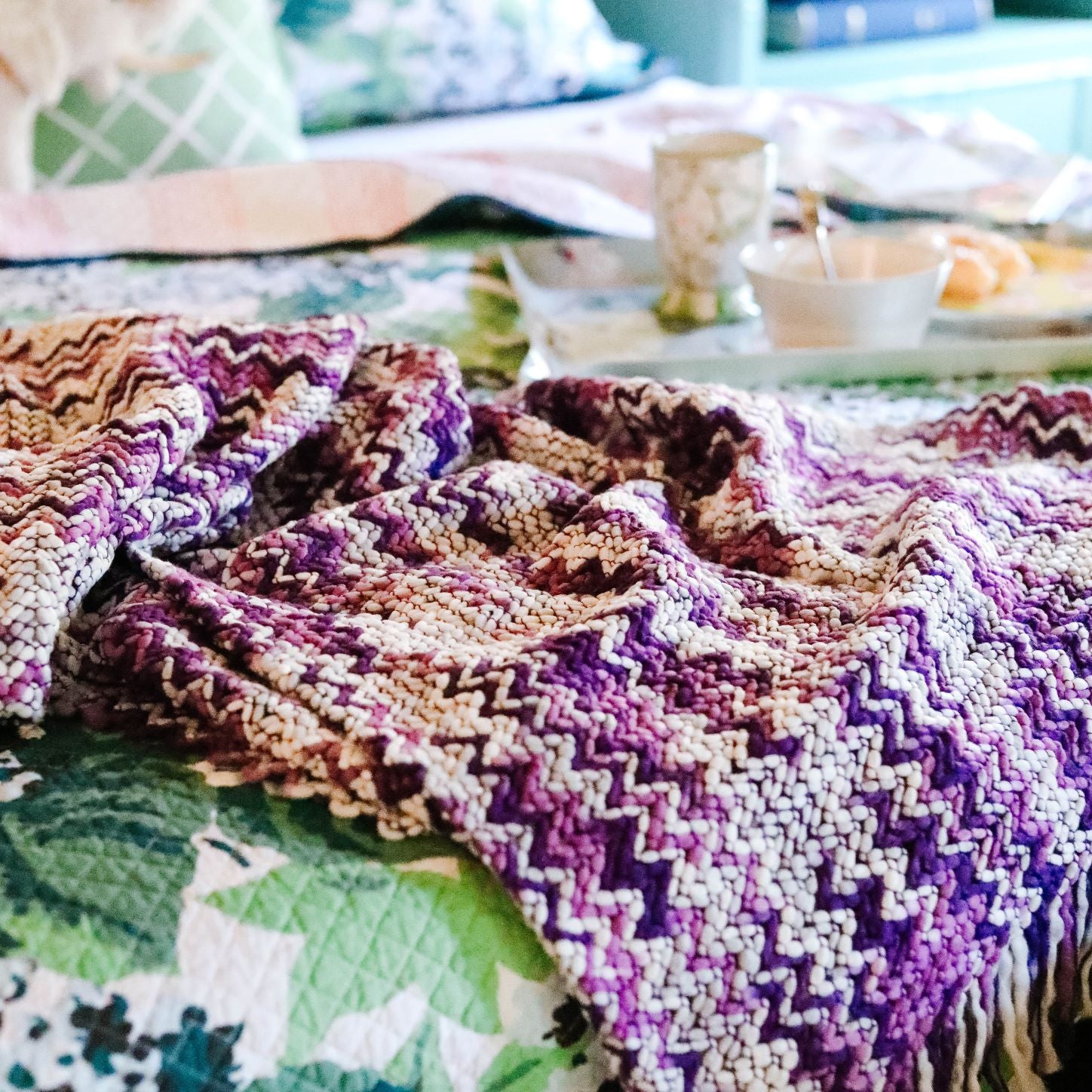 A woven purple throw blanket draped across a bed.