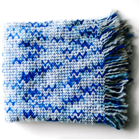 A blue throw blanket with a woven zig zag pattern 