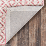 Pink and ivory diamond patterned flatweave area rug displayed on a wood floor, modern geometric woven area rug.