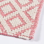 Close-up of pink and ivory diamond patterned flatweave area rug showing textured woven fibers and stitched edge detail.