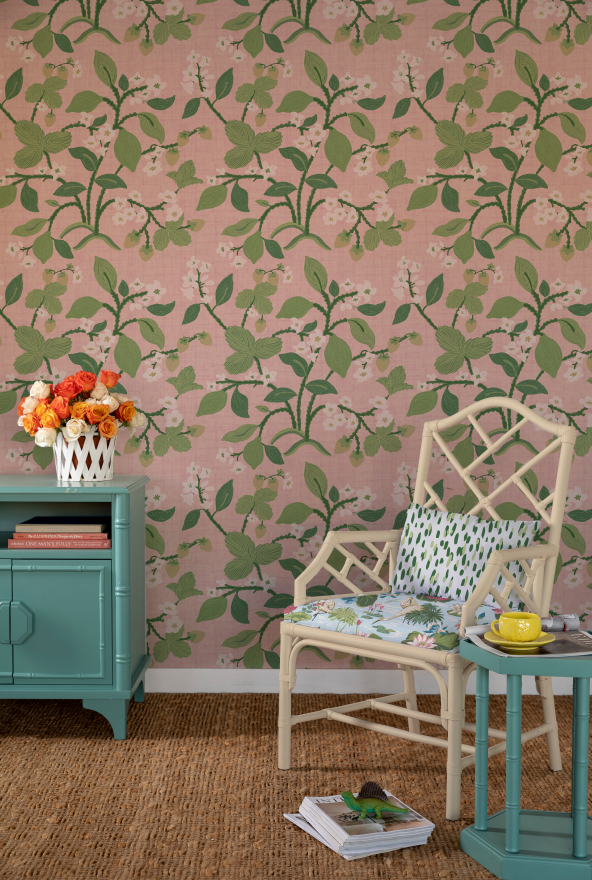 a chair and chest of drawers against a background of green, white and pink wallpaper with strawberry and lemon motifs. 