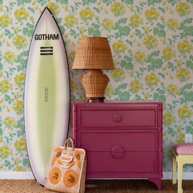 Yellow geranium wallpaper in a room with pink drawers, rattan lamp and a large surfboard. 