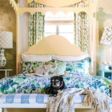 a yellow four poster canopy bed with floral bedding and a black pug dog on a bench at the end.