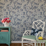 white chair and green chest against a wall of Blue and white chinoiserie wallpaper featuring blue cherry blossom motifs on a light blue background.
