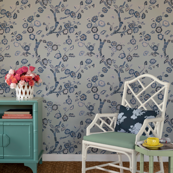 white chair and green chest against a wall of Blue and white chinoiserie wallpaper featuring blue cherry blossom motifs on a light blue background.
