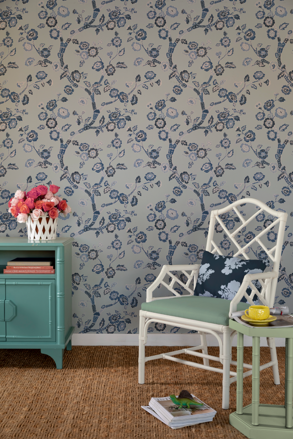 white chair and green chest against a wall of Blue and white chinoiserie wallpaper featuring blue cherry blossom motifs on a light blue background.