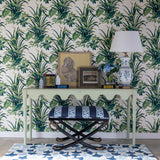 a light green console table topped with a lamp and decorative objects against a background of palm leaf print wallpaper