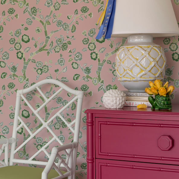 chest, lamp and chair against pink and green chinoiserie wallpaper featuring green cherry blossom motifs on a pink  background. 