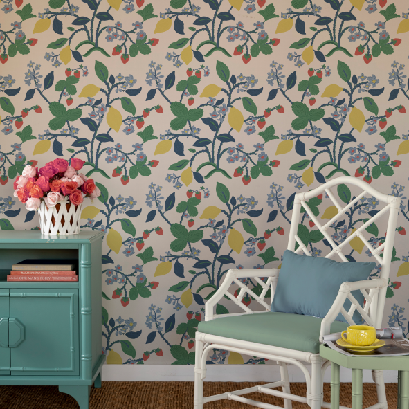 a white chair and green sideboard against a wall featuring colorful strawberry wallpaper.