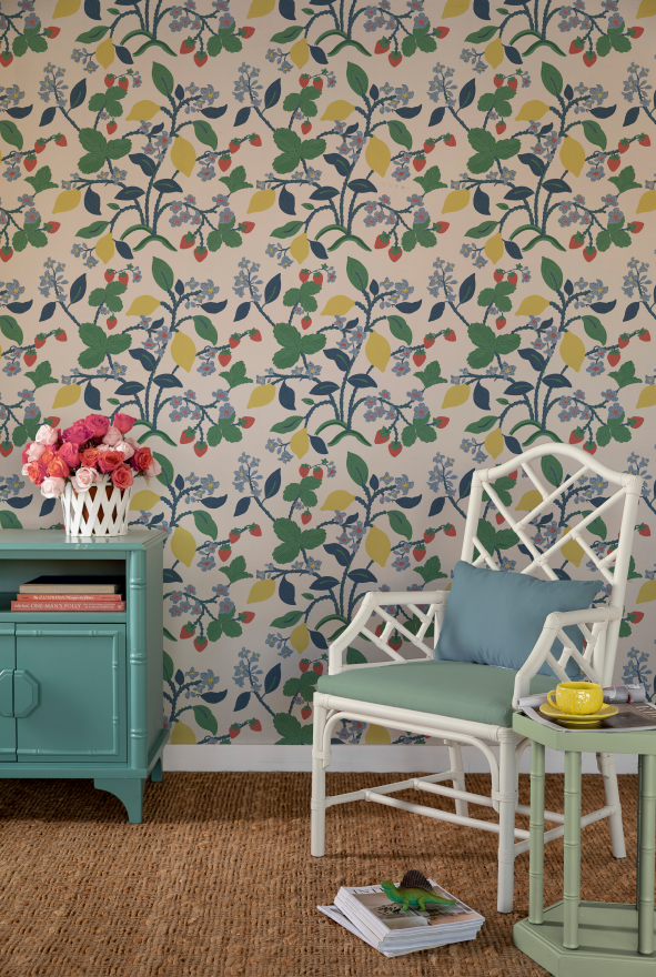 a white chair and green sideboard against a wall featuring colorful strawberry wallpaper.