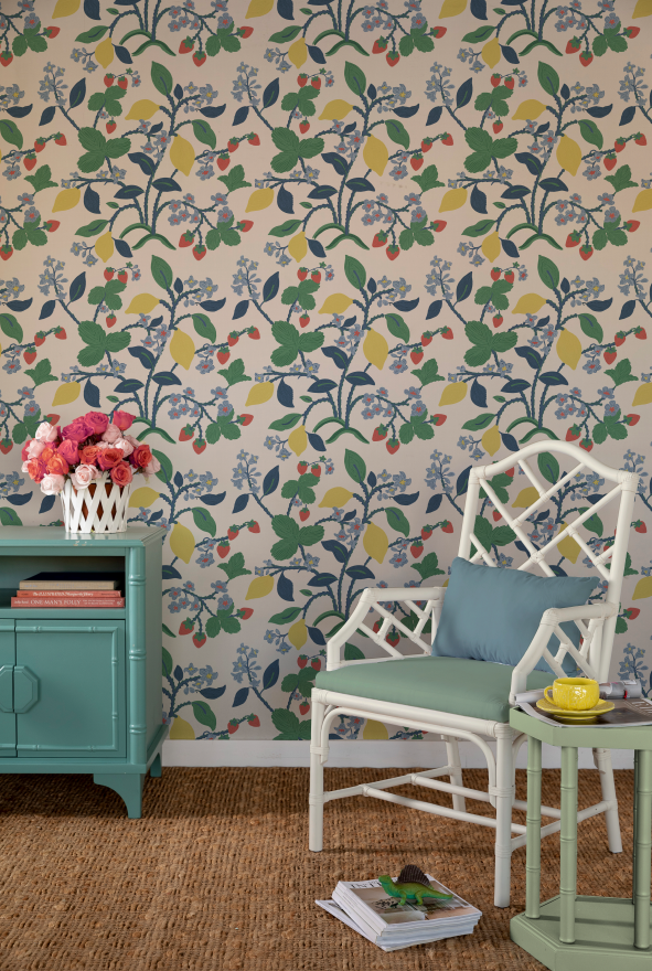 a white chair and green sideboard against a wall featuring colorful strawberry wallpaper. 