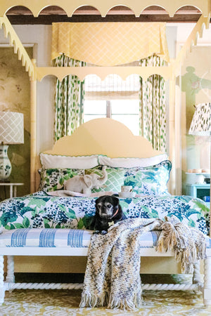 a yellow four poster canopy bed with floral bedding and a black pug dog on a bench at the end. 